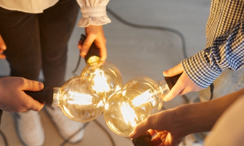 Close up of bright light bulb in the hands of different people